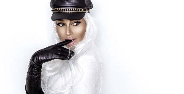 Высокая модель. Женская модель носит черную байкерскую шляпу и длинные кожаные перчатки и позирует на белом фоне. Vogue. - Фото, изображение