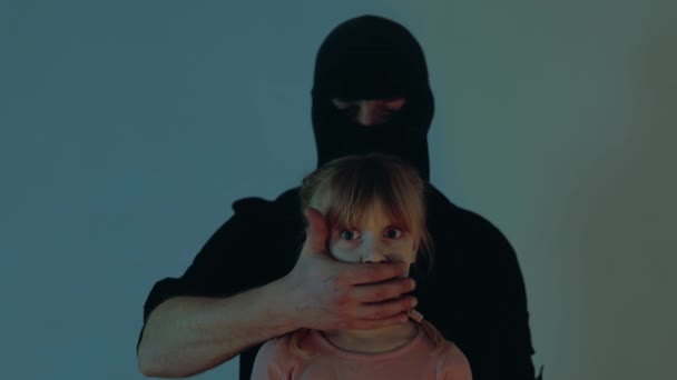 Muž zakrývající ústa vyděšeného dítěte jako rukojmí. Únosce v černé kuklě ukradl malou holčičku. Koncept únosu dítěte. Zpomalený pohyb - Záběry, video