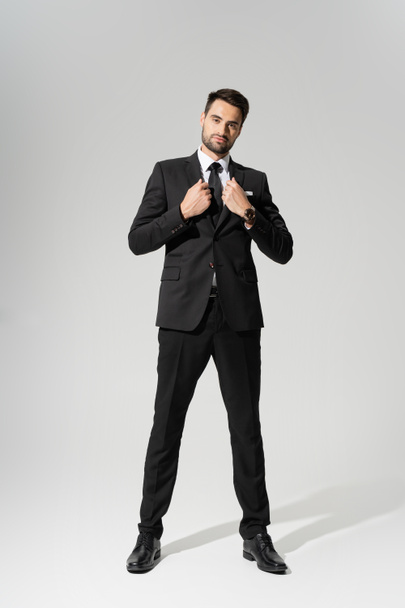 full length on confident businessman in black stylish pantsuit on grey background - Foto, afbeelding