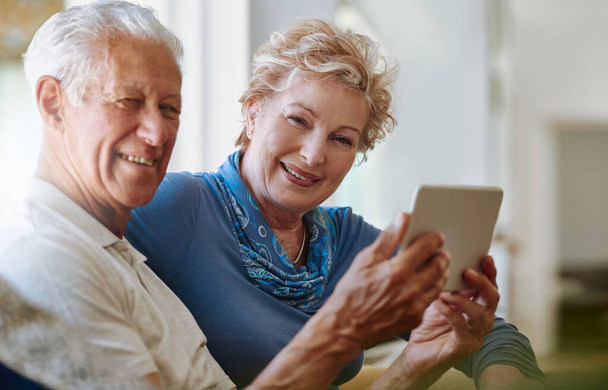 Embracing smart technology with both hands. Portrait of a happy senior couple using a digital tablet together on the sofa at home - Photo, Image