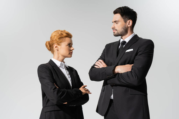 confident businessman looking at serious redhead businesswoman isolated on grey - Photo, Image