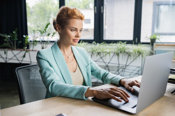 mujer de negocios en blazer elegante escribiendo en el ordenador portátil en la oficina moderna - Foto, imagen