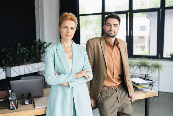 positive business colleagues standing at work desk in modern office and looking at camera - Photo, Image