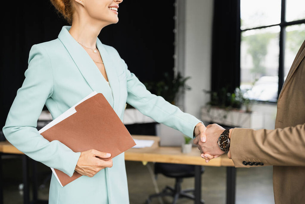 cropped view of happy businesswoman with folder shaking hands with manager in office - Фото, изображение