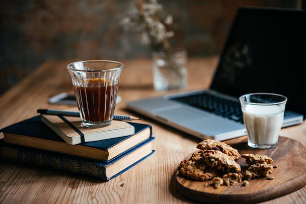 Coffee and some light snacks served during a break with laptop and books in the background. Working from home concept. - Фото, изображение