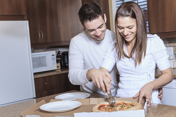 A Happy young couple eating pizza at the kitchen - Fotografie, Obrázek