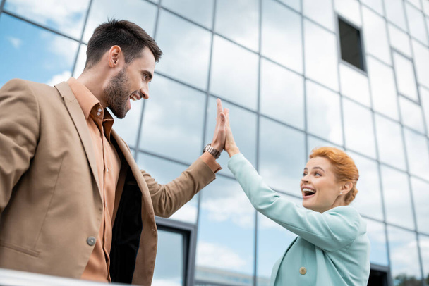 dolblij zakenpartners geven high five in de buurt van modern gebouw op stedelijke straat - Foto, afbeelding