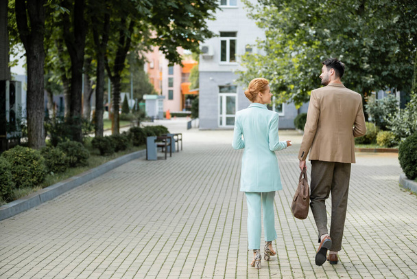 back view of stylish business colleagues talking during walk along green alley in city - Fotoğraf, Görsel