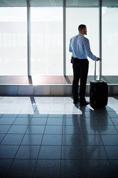 is a well seasoned traveller. a businessman looking through airport windows while on a business trip - Φωτογραφία, εικόνα