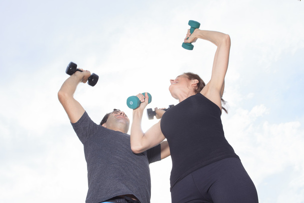 A Young, caucasian couple working out with dumbbells outside - Фото, зображення