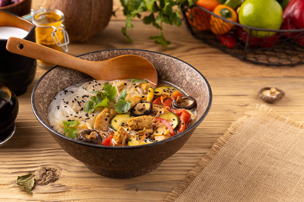 Thai soup with chicken, peppers and mushrooms. With the addition of coconut milk. Served in a classic Asian bowl.  Natural wood in the background. - Foto, immagini