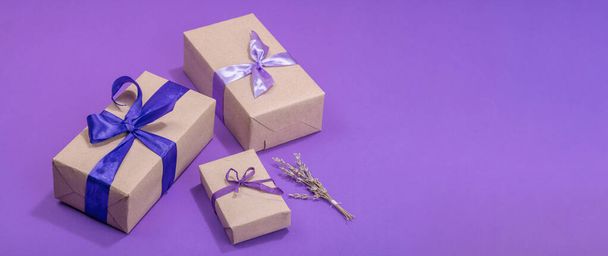 Zero waste gift concept. Wrapped in craft paper surprise box for Anniversary, Mothers or Valentines Day. Happy birthday greeting card, purple background, flat lay, banner format - Fotografie, Obrázek