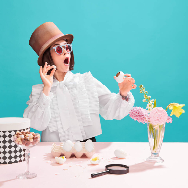Birth of chocolate. Creative photography of young astonished woman in stylish blouse and cylinder hat holding egg with chocolate piece inside. Concept of pop art, creativity, food, inspiration - Photo, image