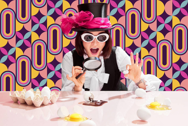 Creating masterpiece. Emotional, excited woman in cylinder and sunglasses looking in magnifying glass on eggs with chocolate spilling out. Pattern multicolored background. Pop art, creativity, food - Fotografie, Obrázek