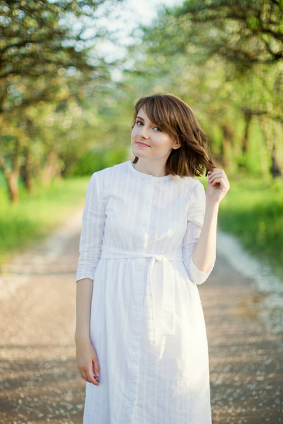 Beautiful caucasian woman in white dress walks in spring blossom garden - Foto, imagen