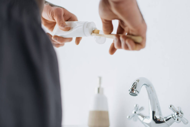 Προβολή ενός Αφροαμερικανού με λεύκη να πιέζει οδοντόκρεμα σε οδοντόβουρτσα κοντά στο νεροχύτη στο μπάνιο  - Φωτογραφία, εικόνα