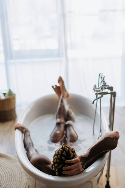 Rückansicht eines afrikanisch-amerikanischen Mannes mit Vitiligo, der zu Hause ein Bad mit Schaum nimmt  - Foto, Bild