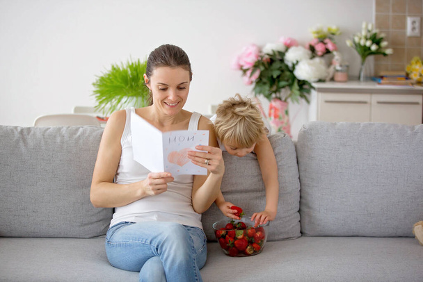 Cute toddler child, giving mom card with heart for Mothers day, mom eating strawberries - Fotoğraf, Görsel