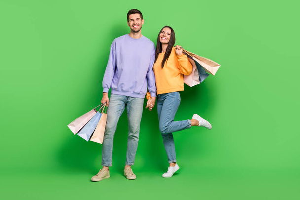 Full length photo of two lovely partners toothy smile hold hands shop packages isolated on green color background. - Фото, изображение
