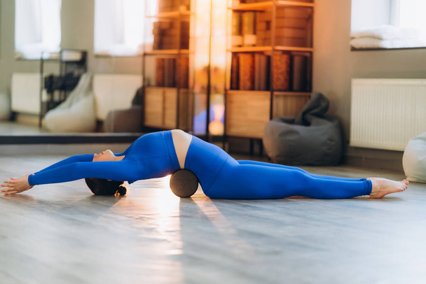 Portrait d'une belle jeune femme européenne faisant du sport en studio. Une fille en legging et un haut bleu est sur son dos sur un bloc d'étirement du dos. Yoga, fitness, sport. - Photo, image