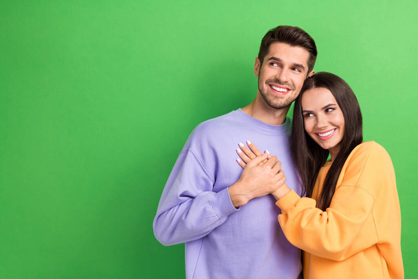 Photo of adorable dreamy boyfriend girlfriend wear sweatshirts cuddling looking empty space isolated green color background. - Photo, Image