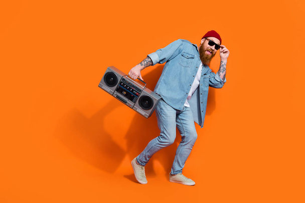 Full length photo of cool positive man wear jeans shirt listening boom box having fun isolated orange color background. - Foto, afbeelding