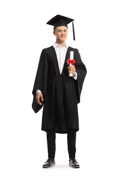Full length portrait of a smiling male student wearing a graduation gown and holding a diploma isolated on white background - Fotoğraf, Görsel