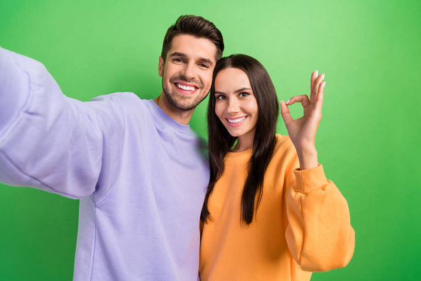 Photo of cheerful attractive lady handsome guy make selfie demonstrate okey symbol isolated on green color background. - Foto, immagini