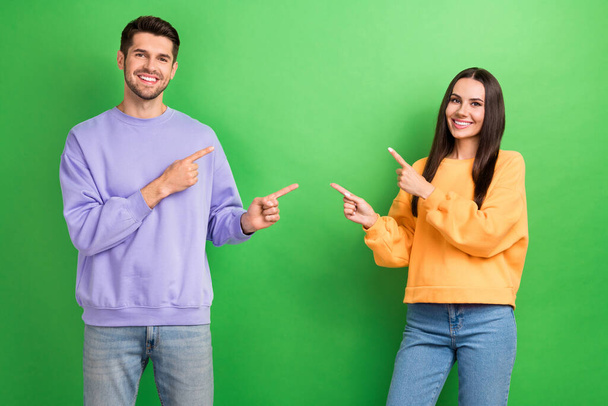 Photo of cheerful positive husband wife dressed sweatshirts pointing empty space isolated green color background. - Fotó, kép