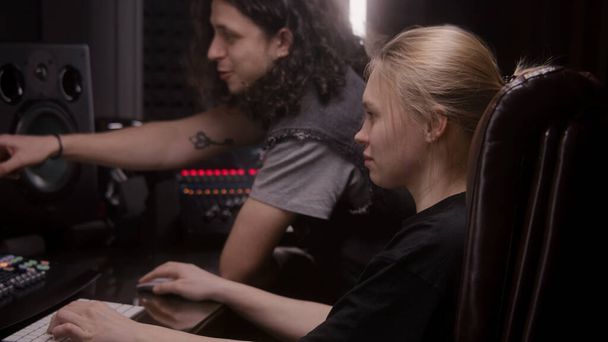 女性のオーディオエンジニアとミュージシャンは、音楽録音室で曲を作成します。サウンドトラックとDAWソフトウェアインターフェイスを示すコンピュータ画面。録音スタジオの近代的な機器。音楽制作. - 写真・画像