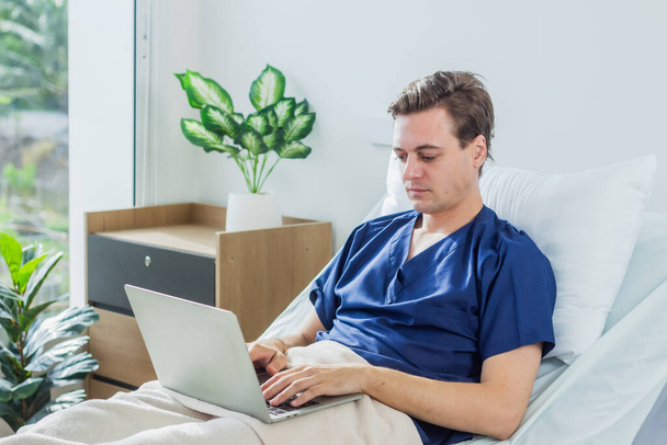 Biały pacjent korzystający z laptopa w pokoju szpitalnym. chory pacjent leżący w szpitalnym łóżku. - Zdjęcie, obraz