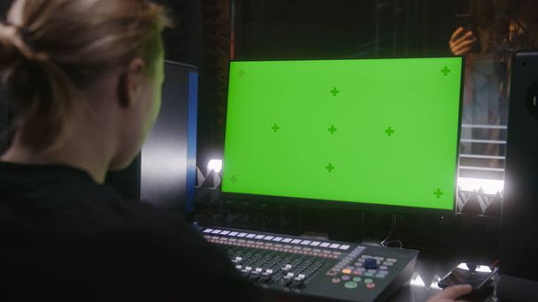Erkek şarkıcı ses geçirmez odada şarkı kaydediyor. Kadın ses mühendisi, yapımcı miksaj yüzeyini kontrol ediyor. Bilgisayar ekranı DAW yazılımını ses parçalarıyla gösteriyor. Ses kayıt stüdyosu. Yeşil Ekran. - Fotoğraf, Görsel