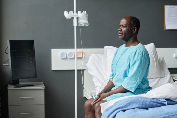 African American elderly man with dropper sitting on bed in hospital ward - Foto, Imagen