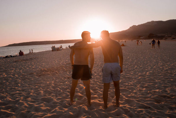 Dwóch młodych przyjaciół spogląda na zachód słońca w piękny letni dzień na plaży.. - Zdjęcie, obraz