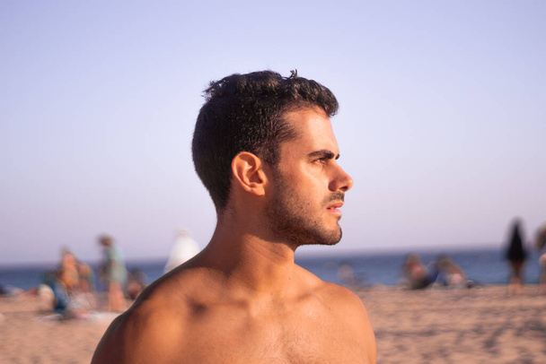 a dark-haired young man looks out to sea on a beach vacation day - Foto, Imagem