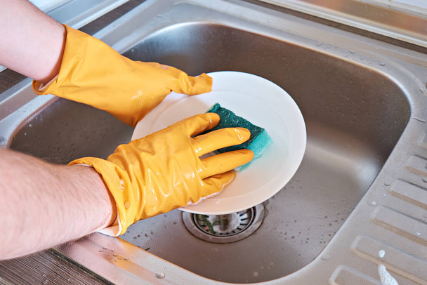 As mãos humanas em luvas protetoras lavam uma chapa com uma esponja de cozinha. - Foto, Imagem