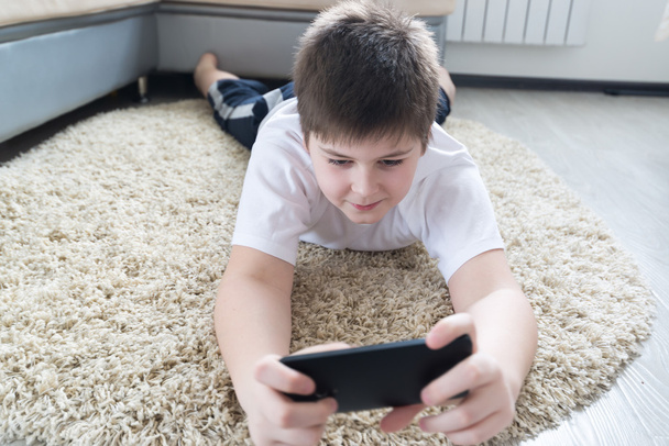 boy with  phone lying on a carpet in the room - Foto, Imagen