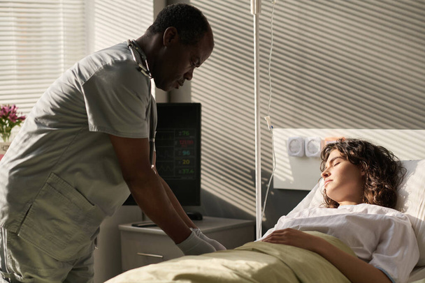 Afroamerikanische Ärztin macht Dropper für junge Patientin, während sie auf Station im Bett schläft - Foto, Bild