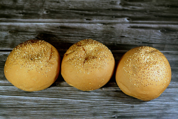 Round hand sized hamburger burger bun baked and covered with sesame seeds, bun is a type of bread roll, typically filled with savory fillings, made from a dough of flour, milk, yeast, butter - Fotoğraf, Görsel