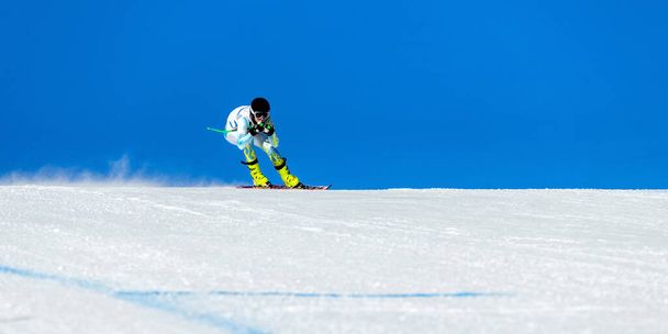 skieur masculin sur piste de ski alpin, piste enneigée sur fond de ciel bleu, jeux de sports d'hiver - Photo, image