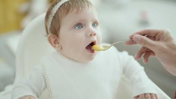 Imádnivaló szőke baba ül etetőszéken eszik otthon - Felvétel, videó