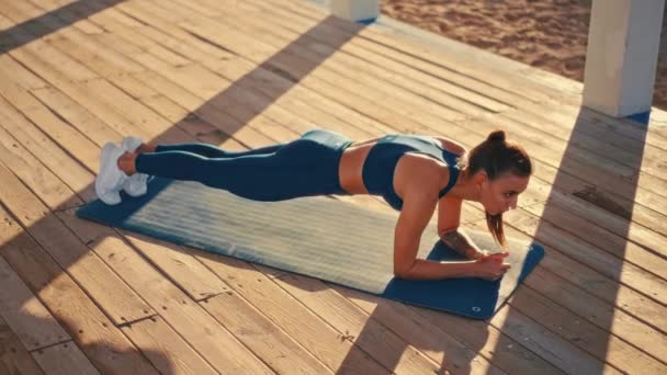 Молода красива жінка в спортивному одязі робить ранкові вправи на гумовому килимку на пляжі. На відкритому повітрі тренування біля моря. Спорт і відпочинок, фітнес і здоровий спосіб життя
. - Кадри, відео