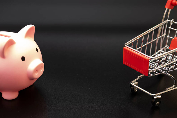 piggy bank in a shopping cart on a black background. us dollars. - Zdjęcie, obraz