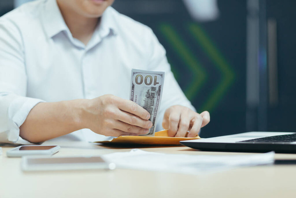 Een close-up foto. Handen van een jongeman die contant geld in een portemonnee stopt, geld telt in het kantoor aan tafel. Financiële toewijzing, bonus, salaris. - Foto, afbeelding