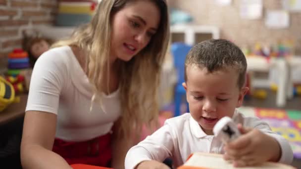 Учителя с мальчиком и девочкой играют с автомобильной игрушкой, сидя на столе в детском саду - Кадры, видео