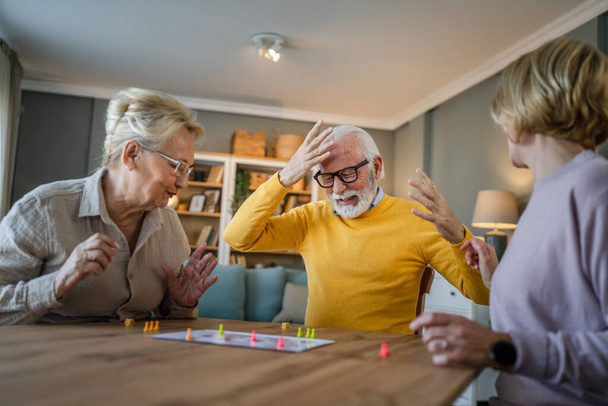 Grupa seniorów mężczyzna i kobieta mąż i żona przyjaciele lub rodzina grać rekreacyjna gra planszowa w domu zabawy emeryt dziadek i babcia spędzają czas wraz z ich dojrzałą córką - Zdjęcie, obraz