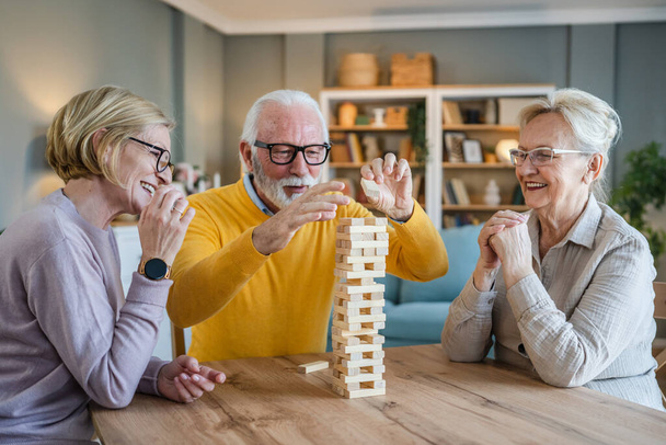Group of senior people man and woman husband and wife friends or family play leisure board game at home have fun pensioner grandfather and grandmother spend time together with their mature daughter - Photo, Image