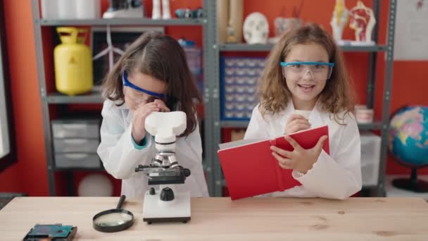 Meninas adoráveis estudantes usando notas de escrita microscópio em sala de aula de laboratório - Filmagem, Vídeo