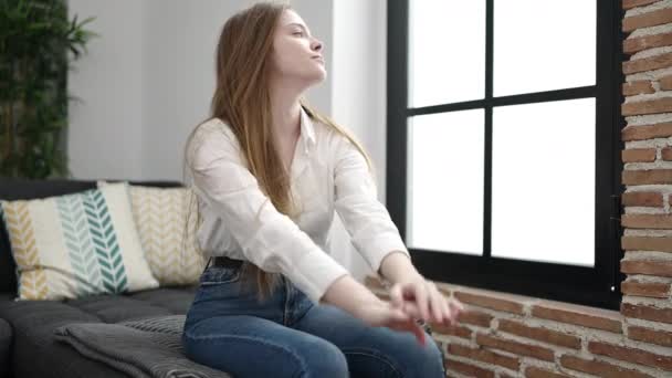 Junge blonde Frau sitzt gestresst zu Hause auf Sofa - Filmmaterial, Video