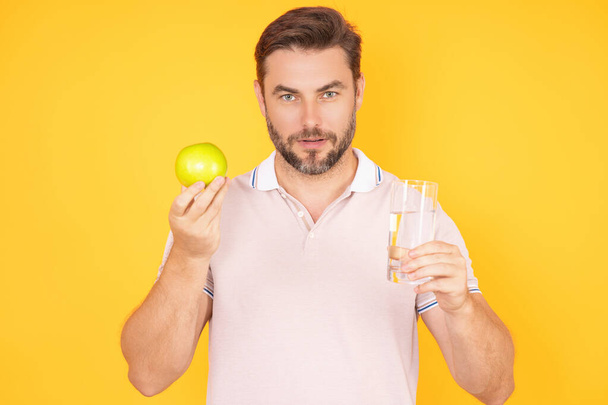 Tasty and juicy apple. Man eating apple, studio portrait. Morning breakfast with vitamin. Man holding apples with healthy teeth. Man biting apple isolated over yellow background - Фото, изображение